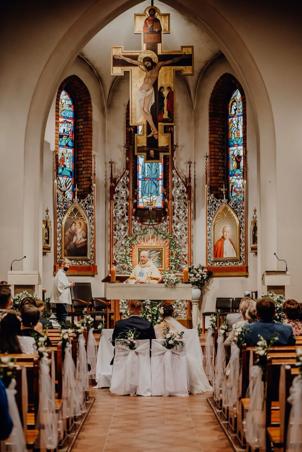 Zdjęcia ślubne w kościele - ceremonia widziana z nawy głównej, ołtarz i witraże