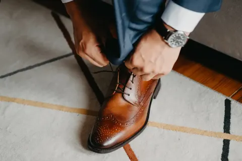 Pan młody zawiązuje sznurowadła brązowych butów typu brogues