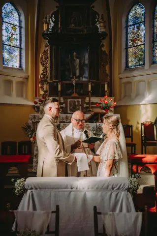 Ksiądz udziela ślubu parze młodej przed zabytkowym barokowym ołtarzem