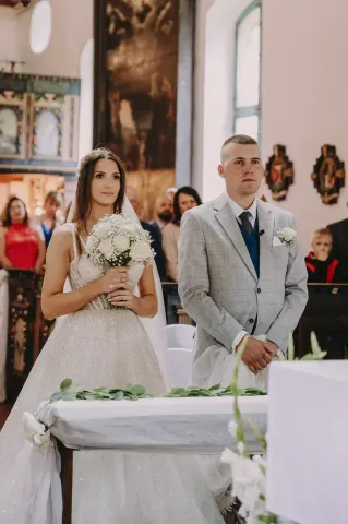 Para młoda stoi przy ołtarzu, panna młoda trzyma bukiet białych róż