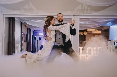 Pierwszy taniec pary młodej w ciężkim dymie i świetle napisu LOVE