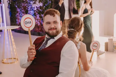 Gość weselny z tabliczką "Ona" podczas zabawy z pytaniami dla pary młodej